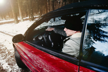 young driver in a red convertible car in a winter forest.