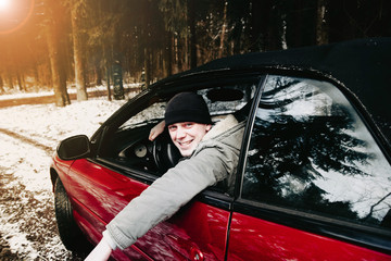 young driver in a red convertible car in a winter forest.