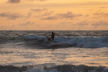 Young people ride on short boards, perform bright tricks on the waves during sunset.