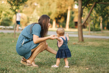 Fototapeta premium First step of adorable little girl in summer park. Mom and daughter walking