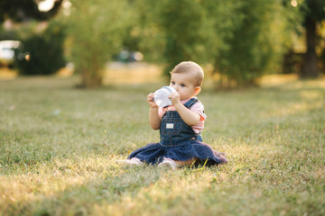 Little baby drink water from baby bottle outside in the park. Baby gir sit on the grass