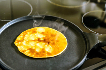 pancake frying pan with crepe pancake cooking on cooker in kitchen