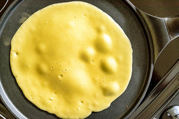 pancake frying pan with crepe pancake cooking on cooker in kitchen