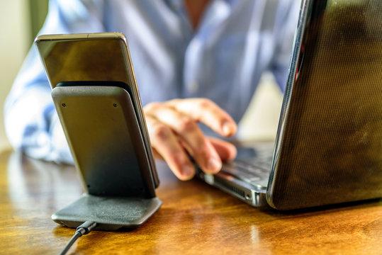 Wireless Phone Charging Stand Over Man Working On Laptop At Home Office