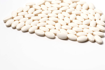 A large number of tablets of white oval-shaped tablets on a white background. Side view