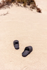 Fototapeta na wymiar Black rubber slippers on the sand near the sea in africa desert