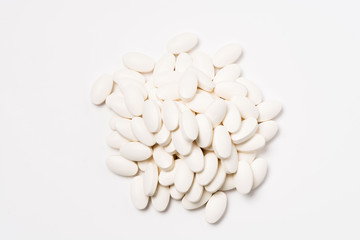 A pile of white oval-shaped tablets on a white background. View from above.