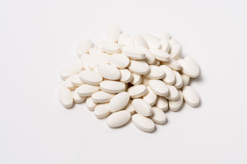 A pile of white oval-shaped tablets on a white background. View from the side