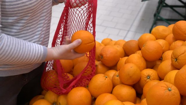 close-up hands of adult woman picking oranges in supermarket and puts fruits on knitted mesh made of eco-friendly materials. selective focus