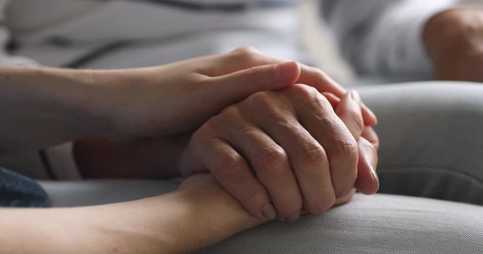Close up young woman stroking hand of middle aged mother, enjoying sweet tender moment. Millennial caregiver or grown up daughter showing support respect to elderly mom, helping in health care.
