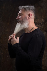 Studio portrait of handsome mature gray-haired bearded man against the dark wall, selective focus