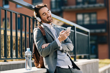 Naklejka premium Happy businessman with headphones using mobile phone outdoors.