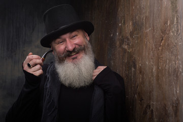 Studio portrait of handsome mature bearded man with a pipe in the black top hat, selective focus
