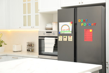Modern refrigerator with child's drawing, notes and magnets in kitchen. Space for text