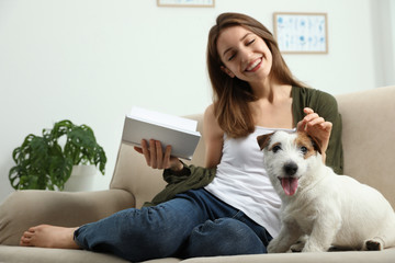 Young woman reading book and her cute Jack Russell Terrier on sofa at home. Lovely pet