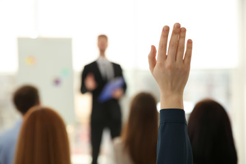 Fototapeta na wymiar Young woman raising hand to ask question at business training indoors, closeup