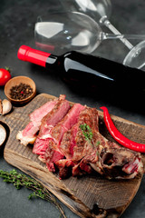 Grilled beef steak with spices and a bottle of wine and glasses on a stone background. Dinner for two