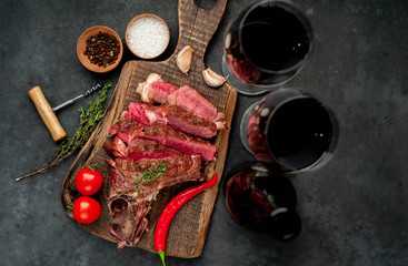 Obraz na płótnie Canvas Grilled beef steak with spices and a bottle of wine and glasses on a stone background. Dinner for two