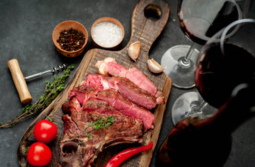 Grilled beef steak with spices and a bottle of wine and glasses on a stone background. Dinner for two