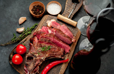 Grilled beef steak with spices and a bottle of wine and glasses on a stone background. Dinner for two