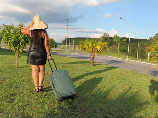 Brazilian woman with black dress and straw hat holding travel bag. Woman going to travel alone