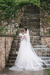 Back view of Gorgeous bride stand on the stairs in elegant wedding dress with bouquet of white flowers in her wedding day