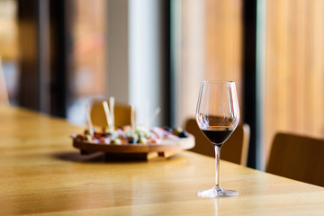 Glass of red wine on the table at home or restaurant in front of the defocused blur appetizer by the window
