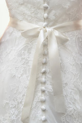 Fototapeta premium Bridesmaid makes bow-knot on the back of brides wedding dress. Preparation of bride for the wedding day before the ceremony. Beautiful lace back of the white dress