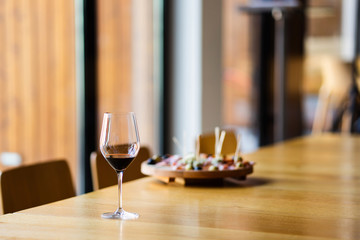 Glass of red wine on the table at home or restaurant in front of the defocused blur appetizer by the window