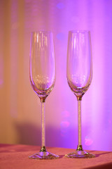 Two empty elegant champagne flutes on a table under artificial purple light, usual recipients for a toast, a welcome or a greeting at a wedding reception, restaurant, formal event or a garden party