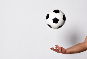 Fototapeta premium Hand of a man with golden wedding ring on his finger is throwing up a soccer ball, isolated on white studio background. Close up