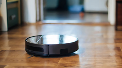 Obraz na płótnie Canvas robot vacuum cleaner removes dust in room on brown floor. vacuum cleaner in ordinary apartment near chairs. modern household wireless device for cleaning house