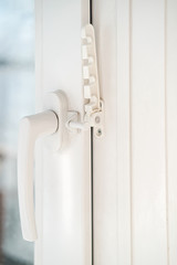 Closed white PVC window, with attached fixing device for ventilation. Close-up.