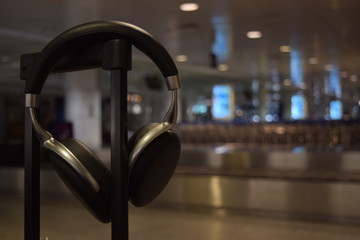 Pair of wireless headphones hanging on a suitcase handle in an airport. Long wait in baggage claim. Music listening.