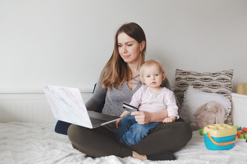 Young Caucasian mother with baby shopping online from home. Stay at home single mom with kid...
