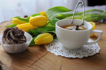 Morning with cup of green tea with marshmallow and yellow tulips on wooden table