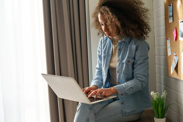 African american teen girl using modern laptop at home. Young mixed race woman user surfing...
