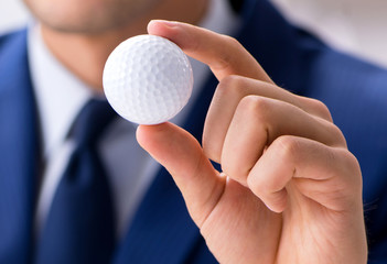 Young businessman with golf ball working in office - Powered by Adobe