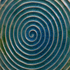 Fototapeta na wymiar The ceramic image of a spiral with light rounds against the background of blue glaze.