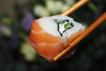 Salmon sushi nigiri in chopsticks over dark background macro shot. Roll with fish and rice in...
