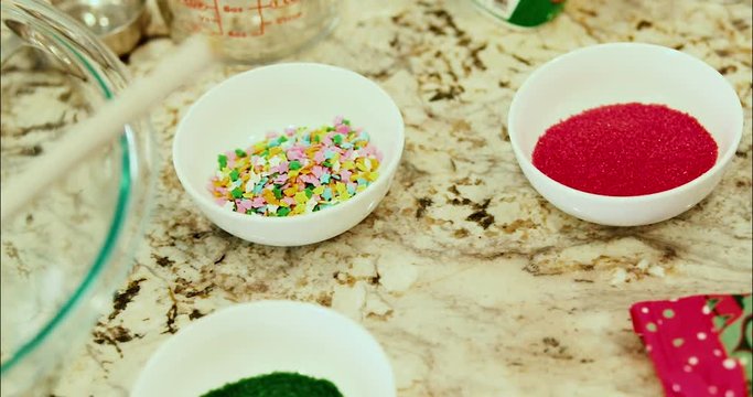 Cookie and baking mix for cookies or a desert pastery. Sprinkles and decorations sit aside a large glass bowl on a marble countertop with a wooden spoon and mix. slow motion 4k