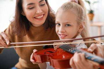 Private music teacher giving violin lessons to little girl at home