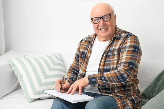 Elderly Man Writing In Notebook At Home