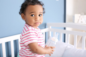 Fototapeta premium Cute African-American baby with bottle of water in crib