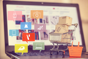 Online shopping, e-commerce experience concept : Box / carton with shopping cart, a grocery basket on a laptop keyboard, depicts consumers / customers / buyer buy goods and service from office or home - obrazy, fototapety, plakaty