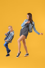 Woman and her little daughter dancing against color background