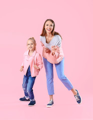 Woman and her little daughter dancing against color background