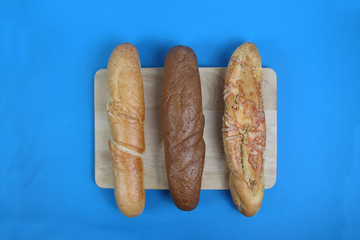 three baguettes on wooden cutting board on blue background flat lay. Horizontal image