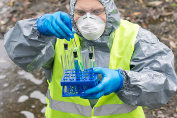 a specialist in protective clothing, a mask and glasses looks at the test tube and determines the...