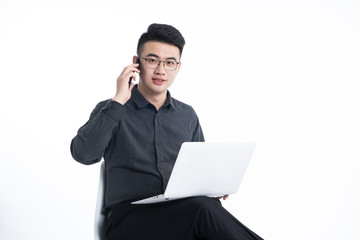 A young Asian man is using his mobile phone and laptop